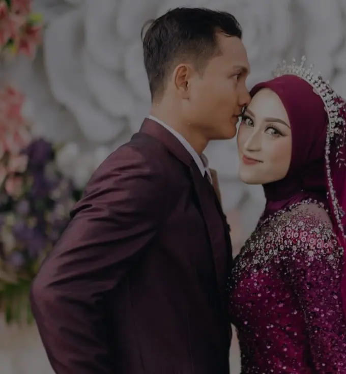 Pasangan pengantin berbusana marun di depan dekorasi bunga