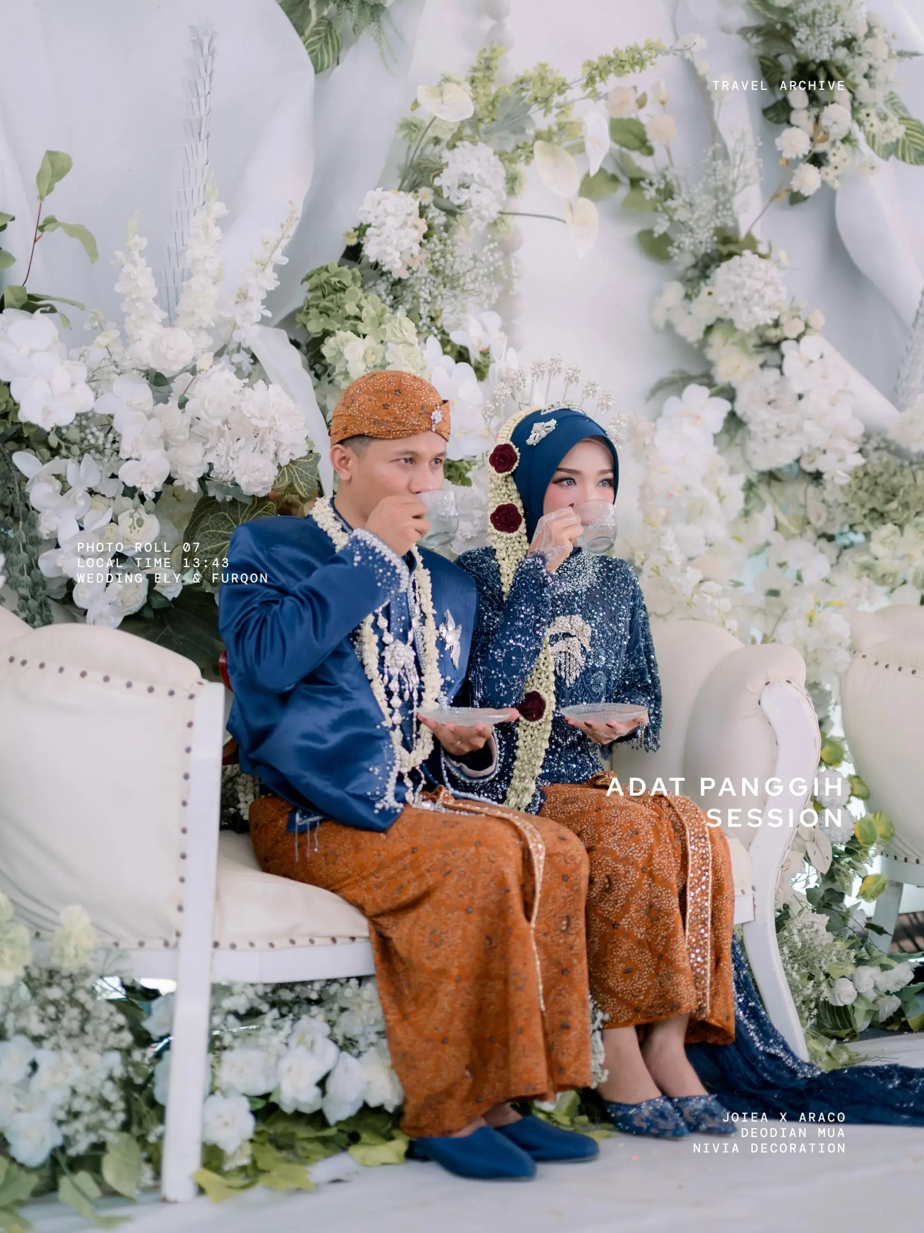 Pengantin berbusana Jawa biru dongker dalam prosesi panggih di pelaminan bunga putih