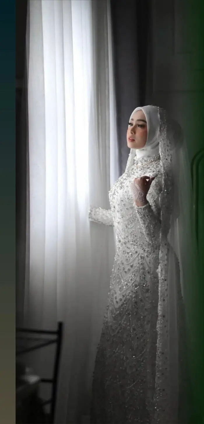 Pengantin wanita bergaun putih berdiri di samping jendela bertirai