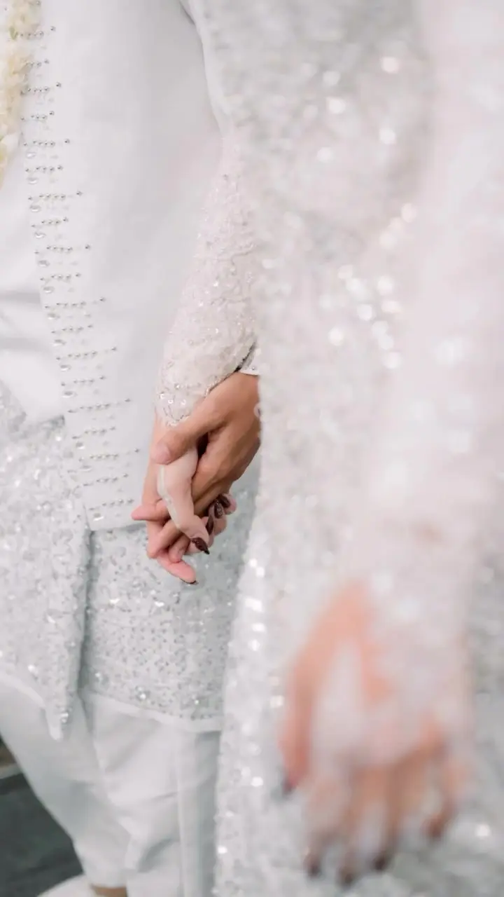 Tangan pengantin bergandengan di antara busana putih berpayet